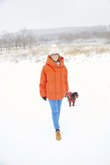 Fototapeta na wymiar Full length shot of a happy woman walking her small dog outdoors on snowy landscape in winter.