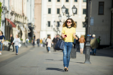 Young beautiful pretty girl walking along the street with phone in hand
