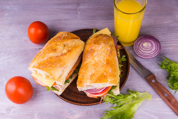 Submarine sandwich with ham, cheese, lettuce, onions and tomatoes on rustic wooden background