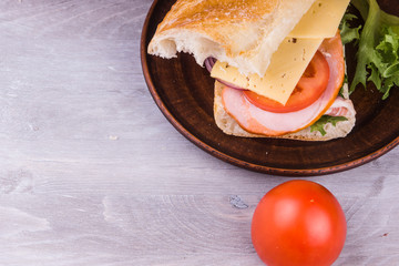 Sandwich with ham, cheese, lettuce, onions and tomatoes on a dark wooden background close-up, copy space