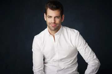 Handsome young man studio portrait. Studio portrait of confident young businessman wearing shirt and looking at camera whle standing at dark background with copy space.