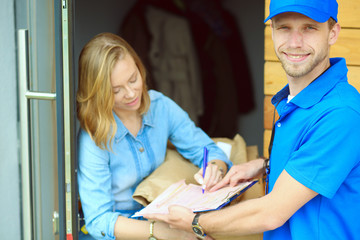 Obraz premium Smiling delivery man in blue uniform delivering parcel box to recipient - courier service concept. Smiling delivery man in blue uniform
