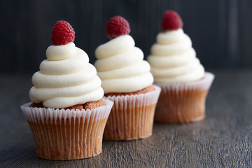 Beautiful cupcakes with fresh raspberries on dark wooden background
