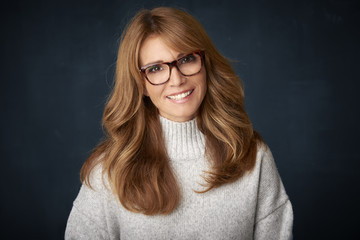 Fototapeta premium Beautiful smiling mature woman portrait. Happy woman wearing turtle neck sweater and looking confidently at camera while posing at dark backgorund. 