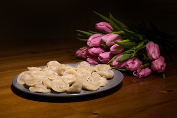 dumplings and a bouquet of pink tulips on a wooden background. tasty and strange feeding to a woman.