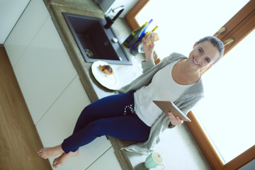 Beautiful young woman using a digital tablet in the kitchen.