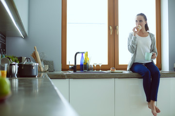 Beautiful young woman using a digital tablet in the kitchen.