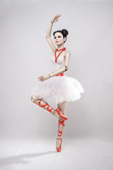 girl as a doll in a ballerina costume with red ribbons on a white background © Mihail