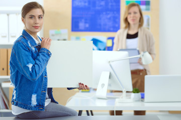 Two young woman standing near desk with instruments, plan and laptop.