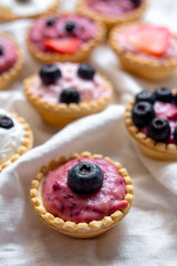 Sweet mini tartlets with cream and berries on white textured background. Simple dessert snack recipe with blueverry and strawberry. Summer food concept.