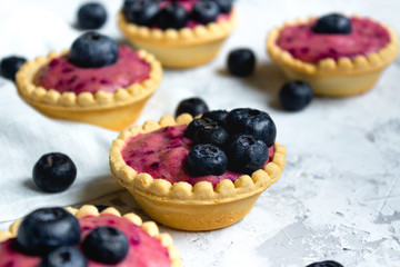 Sweet mini tartlets with cream and berries on white textured background. Simple dessert snack recipe with blueberry. Summer food concept.