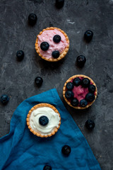 Sweet mini tartlets with cream and berries on a blue linen cloth. Simple dessert snack recipe with blueberry. Summer food concept.