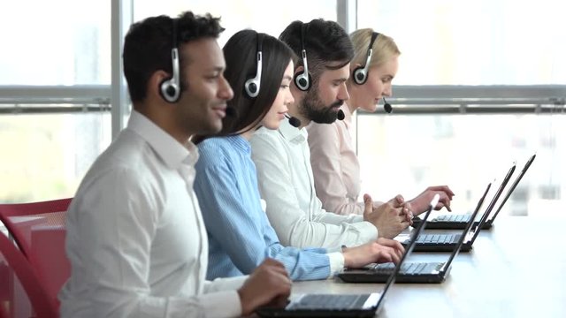 Line of call centre employees working on a laptop computers. Business people group with headphones giving support to customers in bright office.