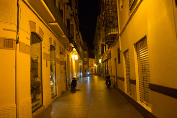 Fototapeta na wymiar Cobblestone street lit with street lamps at night in Malaga, Spain, Europe