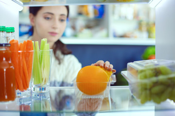 Portrait of female standing near open fridge full of healthy food, vegetables and fruits. Portrait of female