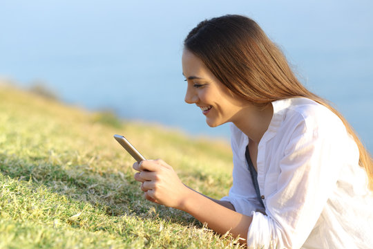 Happy woman using a smartphone lying on the grass