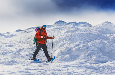 Male adventurer in winter mountain trip having stroll by snow slope, equipped in expedition equipment - snowshoes, sticks, ski mask. Wanderlust, travel, Extreme winter sports and expedition concept.
