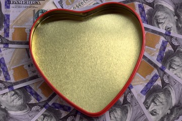 Fototapeta na wymiar A golden heart box with a red outline against the background of hundred-dollar bills spread out in a circle. Concept for the holiday St. Valentine's Day, a gift for the wedding, finance and love.