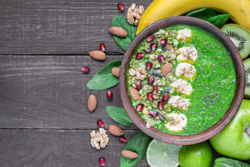 Green fruit and vegetable smoothie bowl topped with granola, banana, pomegranate, pumpkin and chia seeds - obrazy, fototapety, plakaty