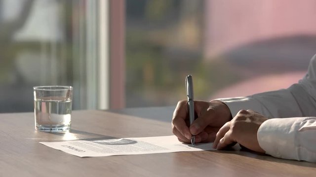 Deal concept, man signing contract and moving away. Peper signing in sunny office. Peper and glass of water on the table.