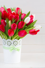 Fresh red tulip flowers bouquet on shelf in front of wooden wall.