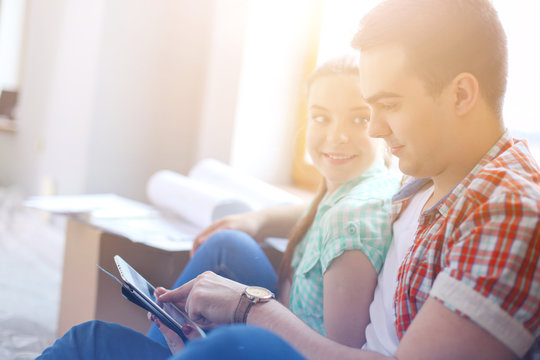 Couple Moving In House Sitting On The Floor With Ipad. Couple