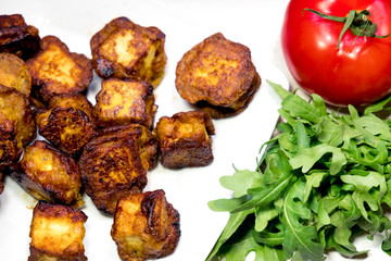 fried Indian slices of cottage cheese on a plate with tomato and rocula
