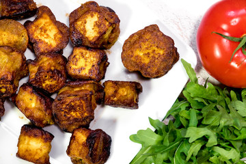 fried Indian slices of cottage cheese on a plate with tomato and rocula