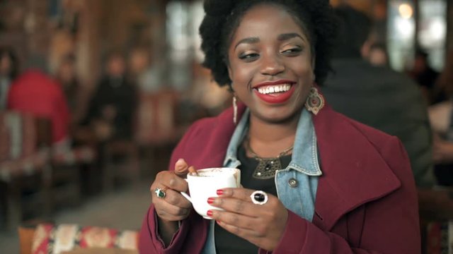 Beautiful African woman tastes sahlep with cinnamon first time and speaks with her friends around her.