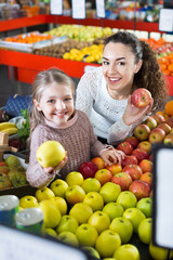 Mother and smiling little daughter choosing seasonal fruits