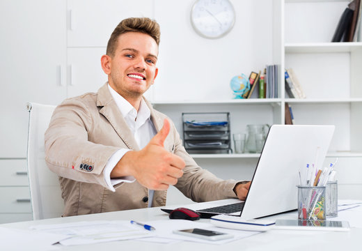 Portrait of businessman showing thumbs up in modern office
