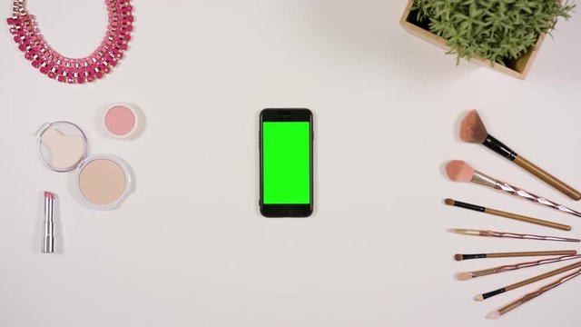 A lady's finger touching a smartphone with a green screen. The phone is on the white table. View from the top. Close-up.