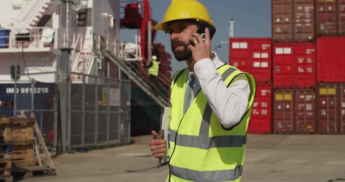 A male worker talking on a mobile phone at a busy shipyard. Shot on RED Epic.