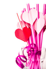 valentine's day holiday. bright pink drinking straws with hearts and a pink ribbon in a glass isolated on white