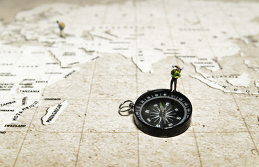 Tiny traveler model stand on compass over brown map 