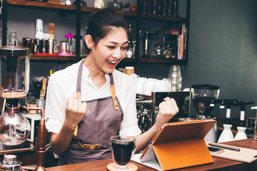 Successful woman barista celebrating with arms up at coffee shop