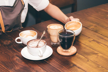 Woman barista holding coffee latte art on wooden table in coffee shop