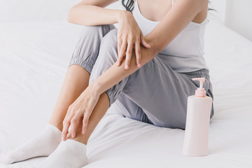 Beautiful woman sitting on bed and touching her skin for applying cream