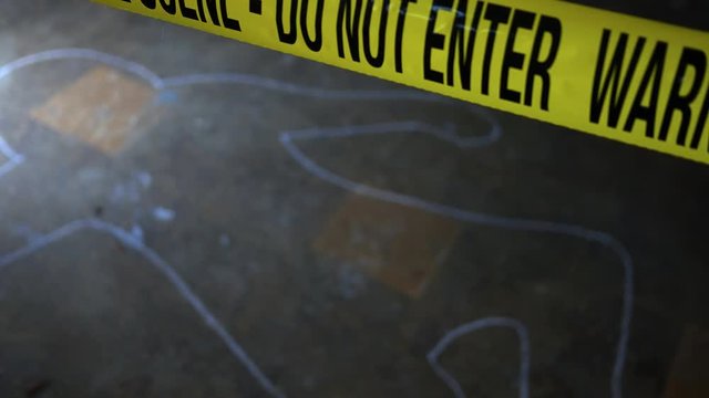Defocused chalk outline at crime scene with police yellow tape in foreground