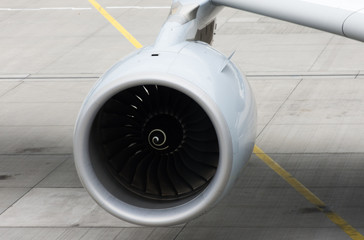 Close Up of a Plane Engine beneath the plane's wind with the tarmac below.
