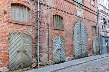 City view of old cobblestone street and vintage brick wall in need of repair and wooden door, Riga Latvia