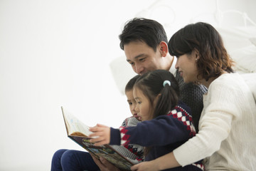 親子四人。父が子どもに絵本を読み聞かせている。