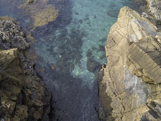 drone shot of a man climbing a rock in the ocean