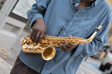 A black saxophone player wearing a denim shirt. He is holding the gold colored sax at an angle at...