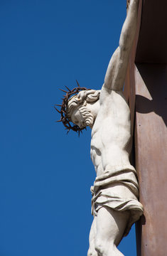 A statue of the crucifixion with Christ on a cross. Photographed against a deep blue sky in Avignon France.