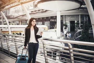 Beautiful young businesswoman walking outside public transportation station. Businesswoman traveler with suitcase on the way to the airport.