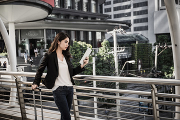 Beautiful young businesswoman walking outside public transportation station. Businesswoman traveler with suitcase on the way to the airport.