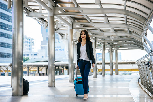 Beautiful young businesswoman walking outside public transportation station. Businesswoman traveler with suitcase on the way to the airport.