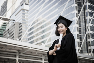 Portrait of young female graduates in square academic cap smiling happy holding diploma against building.