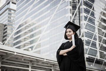 Portrait of young female graduates in square academic cap smiling happy holding diploma against building.